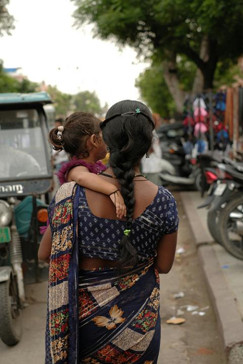 A woman carries a child down a street. (Unsplash/Ravi Sharma)