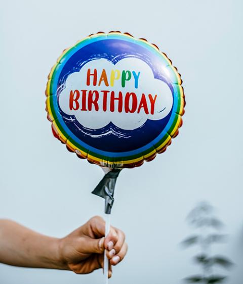Hand holding a balloon saying happy birthday (Unsplash/Markus Spiske)
