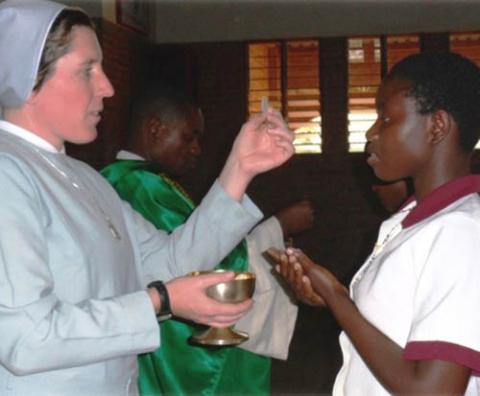 Sister Dwyer in foreground, holding a host and a chalice; in front of her a young student and behind her a priest.