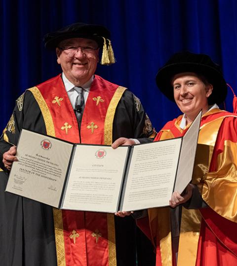 La hermana Dwyer posa con su diploma de reconocimiento honorífico, vestida con toga y birrete.