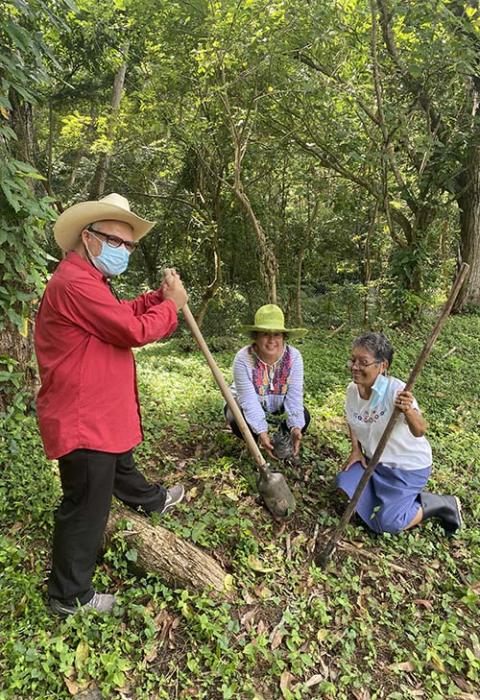 La hermana Trochez descansa, en cuclillas junto a un líder comunitario, y un activista ambiental (de pie) luego de un trabajo voluntario en una granja.