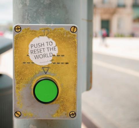 Sticker on lightpost by a button that says "Push to reset the world" (Unsplash/Jose Antonio Gallego Vazquez)