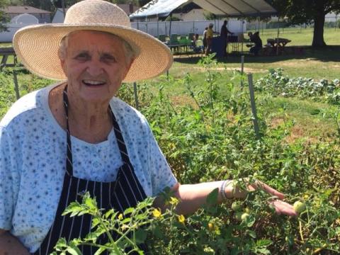 Jeanne Clark in a garden, wearing a straw hat and holding produce