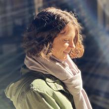 A white woman in a green shirt and white scarf stands in profile, her face to the sun