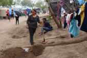In the Matamoros camp on the Mexican side of the U.S. border, Esmeralda, a community leader from Honduras, pauses in wielding a pickaxe, digging a ditch to keep water runoff from her improvised kitchen from muddying the path below. (GSR/Tracy L. Barnett)