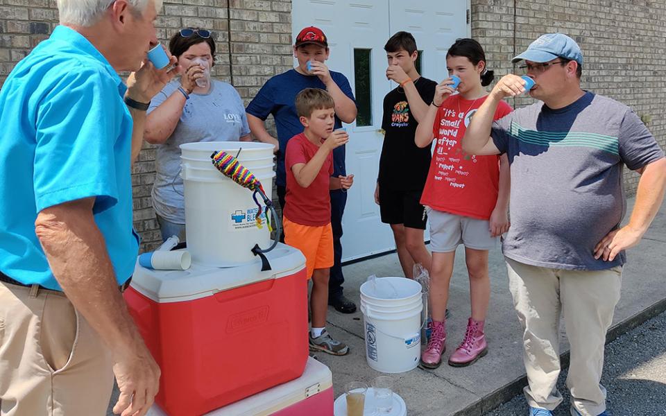 Arnie LeMay of Water With Blessings, left, drinks a cup of filtered creek water Aug. 9 in Chavies, Kentucky, after demonstrating the Sawyer PointONE water filter to volunteers at First Church of God. (CNS/Handout via The Record)
