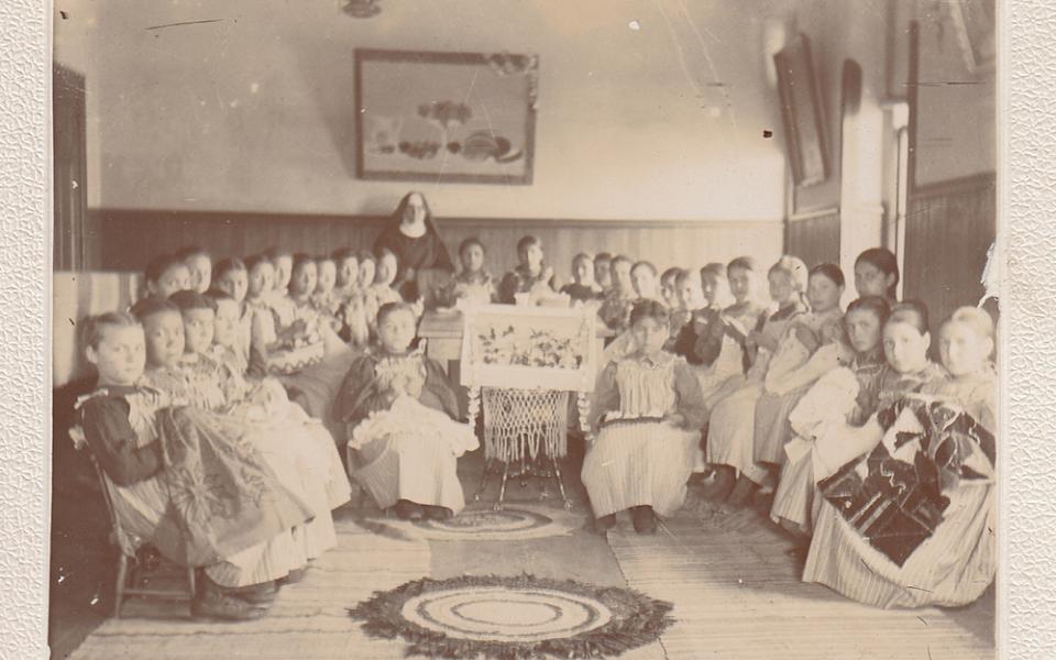 Female students show their handiwork at St. Benedict's Mission School on the White Earth Indian Reservation in Minnesota in the 1890s. ("Work room at St. Benedict's Mission School," College of Saint Benedict/Saint John's University Libraries,  https://csbsjulib.omeka.net/items/show/928)