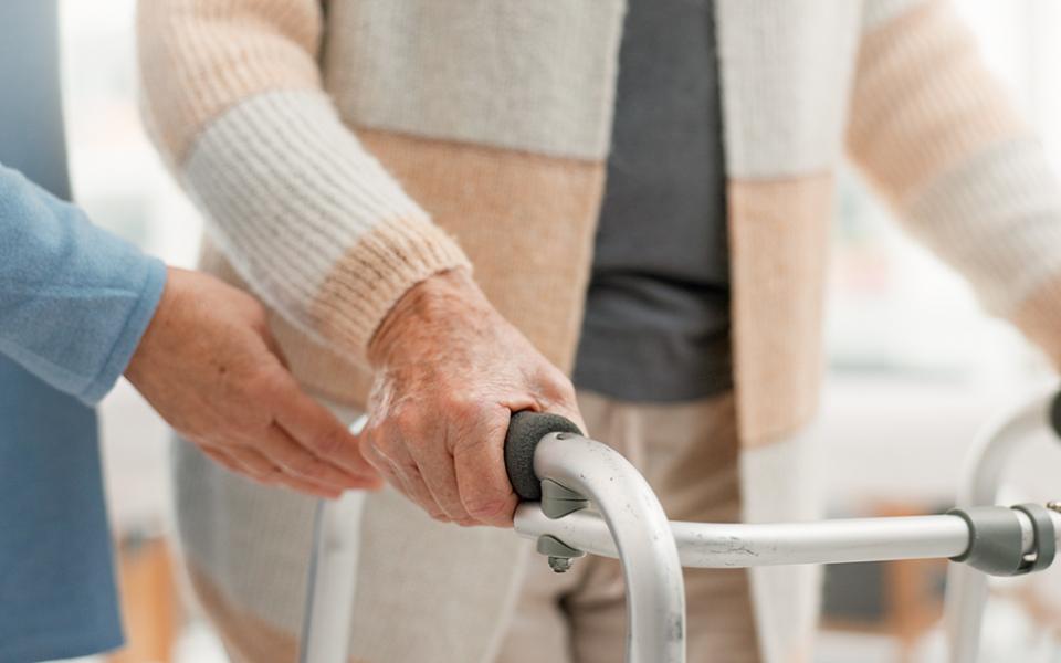 A person uses a walker with a health care worker assisting (Dreamstime/Yuri  Arcurs)