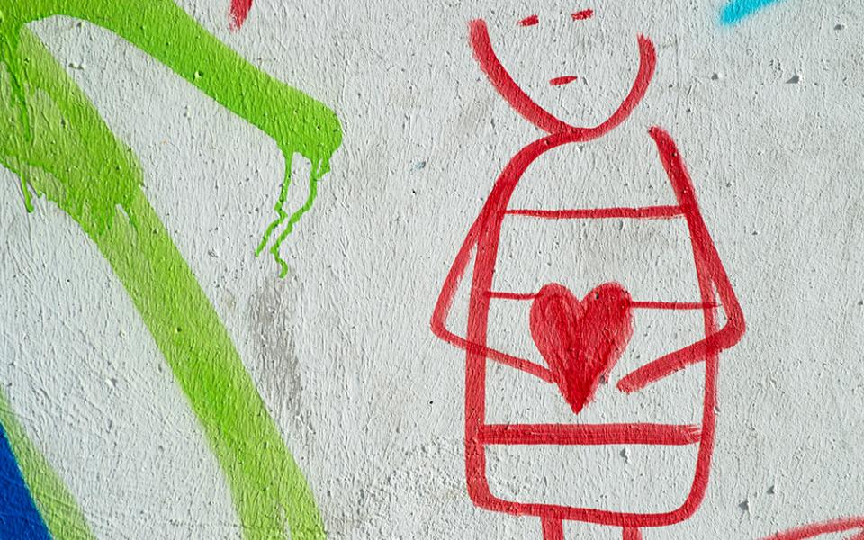 In a drawing illustration, a person with a blank expression cradles a heart. The drawing is done in red, with the heart colored in. Lines of green and blue are also visible against a white background. (Unsplash/Eduardo Goody)