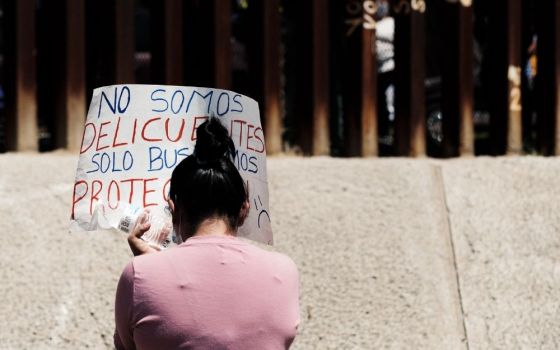 A woman holds a poster at an Aug. 6 border wall encounter at the U.S.-Mexico border, which was organized by the Save Asylum coalition to protest the dismantling of the asylum process. Kino Border Initiative is one of the coalition's supporting organizatio