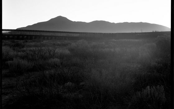 Twilight in Naco, Arizona, extends a haze against its border wall, a "scar on the landscape," as Elmaleh saw it: "Beautiful mountains, vast desert, difficult to cross, and then this massive 30-foot wall is part of the landscape." (© Lisa Elmaleh)