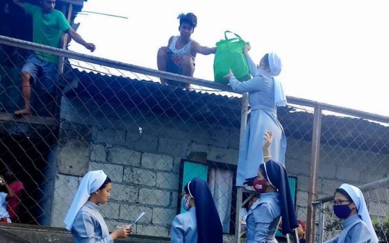 Catholic sisters in the Philippines hand bags of food over a fence to day laborers