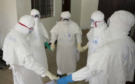 Health workers wearing protective equipment pray at the start of their shift at an Ebola treatment center in Monrovia, Liberia, on Sept. 30, 2014. (CNS / WHO / Christopher Black, handout via Reuters)