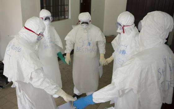 Health workers wearing protective equipment pray at the start of their shift at an Ebola treatment center in Monrovia, Liberia, on Sept. 30, 2014. (CNS / WHO / Christopher Black, handout via Reuters)