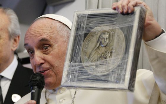 Pope Francis holds up a medallion of St. Therese of Lisieux aboard the papal plane Jan. 15, 2015. (CNS/Paul Haring)