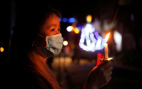 A woman wearing a protective face mask holds a candle in her home while watching Easter Mass via livestream near Hanoi, Vietnam, April 12, 2020, during the COVID-19 pandemic. (CNS/Reuters/Kham)