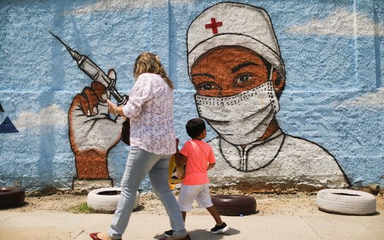 A woman and child walk past a painting on a wall March 12 in Rio de Janeiro during the COVID-19 pandemic. (CNS/Reuters/Pilar Olivares)