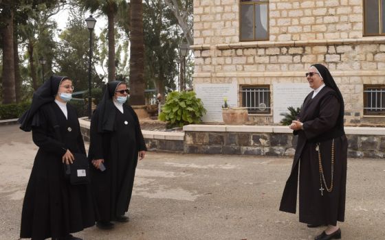 Three nuns in habits meet outside of a stone building