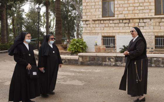 Three nuns in habits meet outside of a stone building