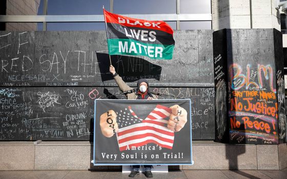 A demonstrator holds a Black Lives Matter flag and another sign April 6 outside the Hennepin County Government Center in Minneapolis on the seventh day of the trial of former police officer Derek Chauvin. (CNS/Reuters/Nicholas Pfosi)