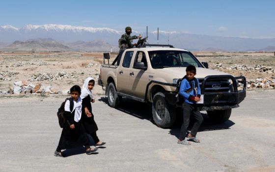 Schoolchildren walk past an Afghan National Army soldier keeping watch at a checkpoint on the outskirts of Kabul, Afghanistan, April 21, 2021. (CNS/Reuters/Mohammad Ismail)