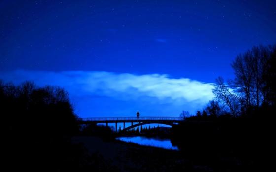 a person stands alone in the center of a bridge at night 
