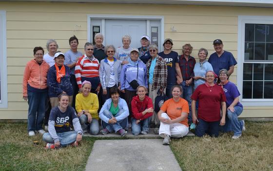 A group of people poses for a photo outside of a yellow house