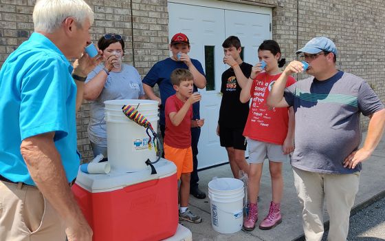 Arnie LeMay of Water With Blessings, left, drinks a cup of filtered creek water Aug. 9 in Chavies, Kentucky, after demonstrating the Sawyer PointONE water filter to volunteers at First Church of God. (CNS/Handout via The Record)