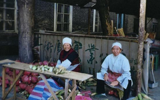 2 sisters sit outside preparing food