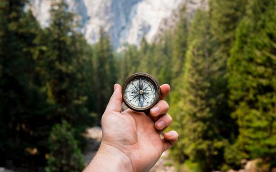 A hand holds compass against background of trees.
