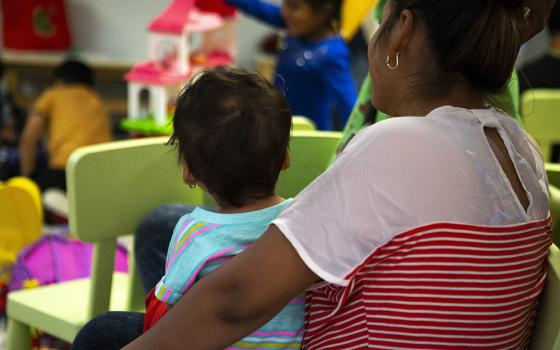 A Central American woman, who was recently released from U.S. custody, holds her child July 1, 2018, as they watch other immigrant children play at a Catholic Charities-run respite center in McAllen, Texas. (CNS/Chaz Muth)