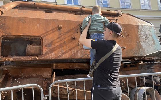 A child gets some help to look at what's left of a Russian tank Sept. 2, 2022 in Rynok Square in Lviv, Ukraine. It was part of a display of tanks and other Russian equipment destroyed by Ukraine's armed forces in the conflict that began Feb. 24, 2022. (Rhina Guidos)