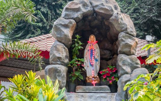 Statue of Mother Mary under stone arch in a garden