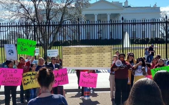 Protesters stand with signs outside fence in front of White House.