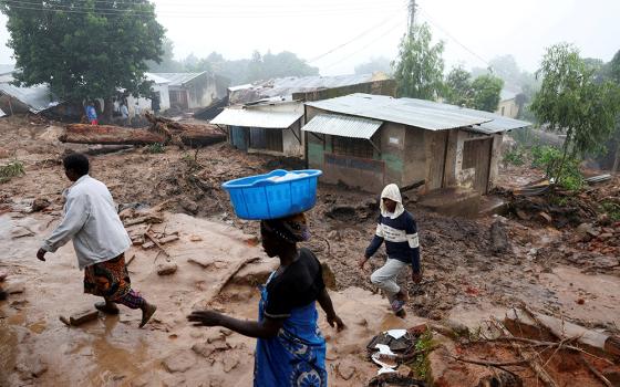 People walk through mud in a damaged residential area