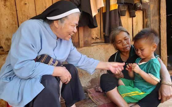 Mary Queen of Peace Sr. Teresa Nguyen Thi Bich offers candy to a grandchild of Mary Ly at her dilapidated house in the Vietnam Central Highlands. The Se Dang ethnic woman, 65, has 12 children who grow rice and coffee for a living. (Joachim Pham)