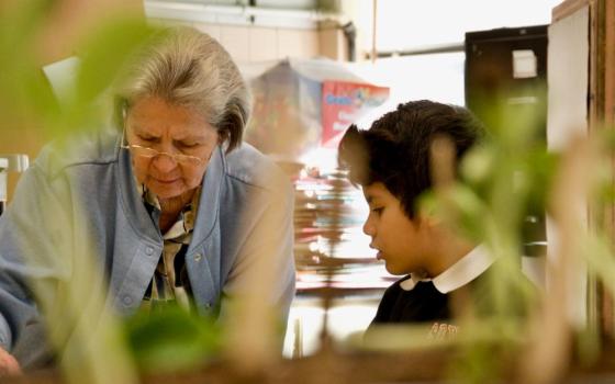 Mercy Sr. Joan Serda works with kindergartner Max on March 16 at St. Pius X Catholic School in Mobile, Alabama. The two are seen through bean-plant seedlings students are growing in the classroom. (GSR photo/Dan Stockman)
