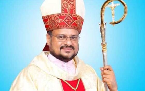 A light-skinned Indian man wears a red and white mitre and holds a crozier