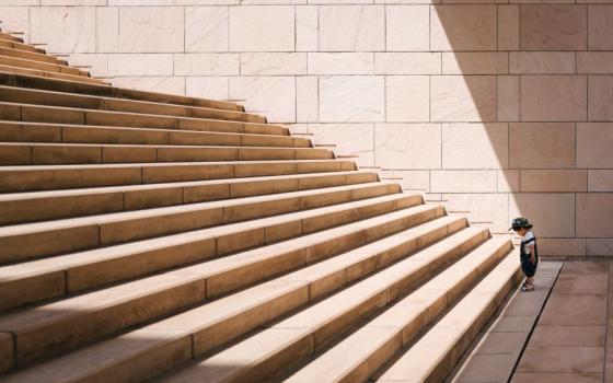 A small child stands at the bottom a large staircase.