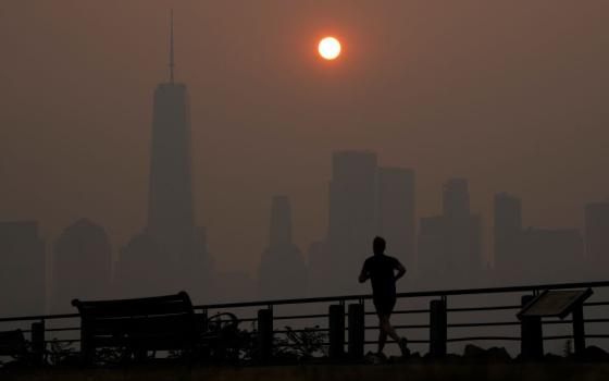 A man runs in front of the sun rising over the lower Manhattan skyline in Jersey City, N.J., on June 8. Intense Canadian wildfires are blanketing the northeastern U.S. 