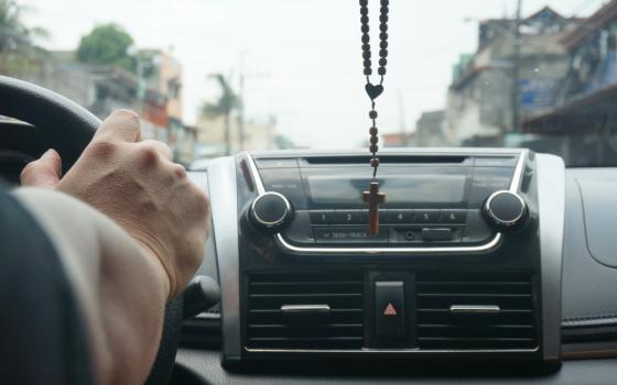 A person driving in a car with a rosary hanging from the rearview mirror (Unsplash/Darla Dela Rosa)