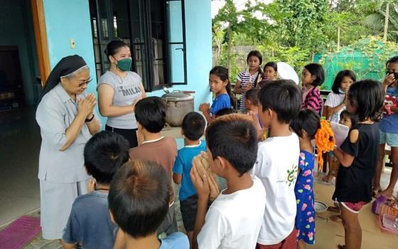 Missionary Benedictine Sr. Edita Eslopor, with the Philberth Foundation scholar volunteer, leads children from a nearby barangay in the Philippines in prayer before their meal. (Courtesy of Edita Eslopor)