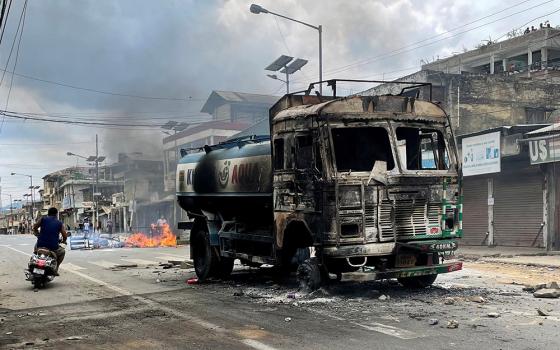 A man rides a scooter past a destroyed water tanker in Manipur, India, May 4, that was set on fire during a protest by tribal groups. The ongoing clash, which began May 3, is between the majority Meitei community (who are mostly Hindu) and Kukis, one of the tribes in the state, most of them Christian). (OSV News/Reuters)