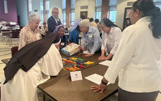 Sisters stand around a table working on a project that involves colored blocks.