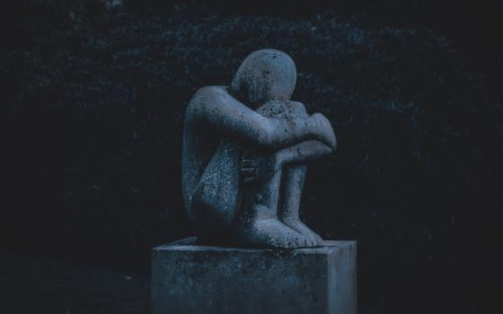 Sculpture of a person crouched, with knees up, arms and head down