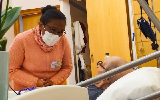 Nurse wearing a mask cares for a patient in hospital bed.