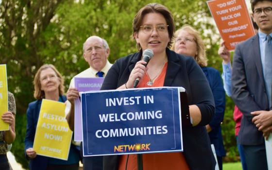 Eilis McCulloh speaks into a microphone in front of sign that reads: "Invest in welcoming communities."