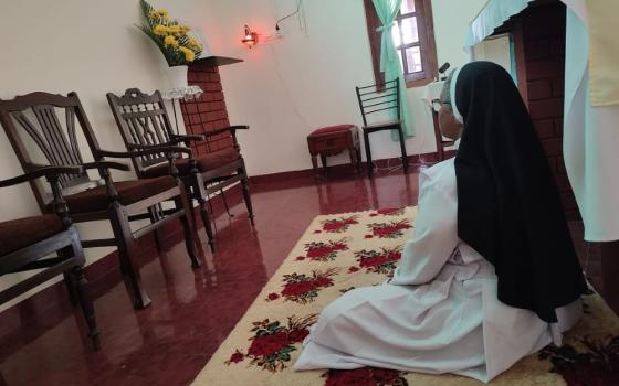 A nun is seen from the back, sitting and praying.