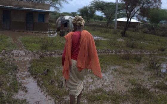 A woman walks through puddles toward a building. 