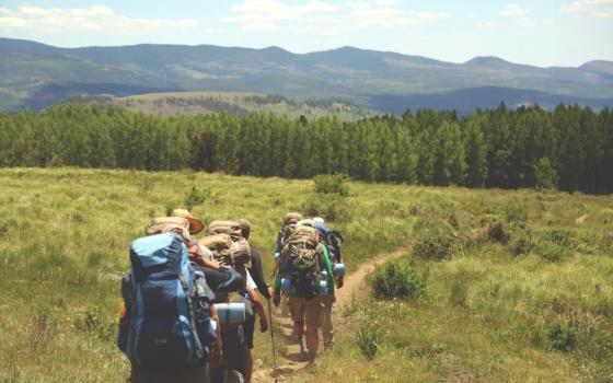 A group of people with backpacks walking on a path amid grass and trees ahead.